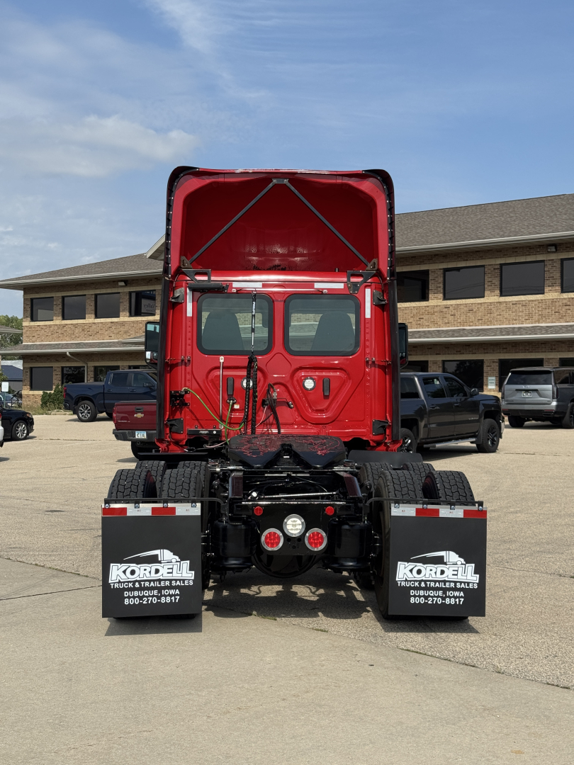 Truck rear view showing red cab rear doors, chassis, mud flaps, and lights; Freightliner Cascadia 116 exposed in a dealership lot.