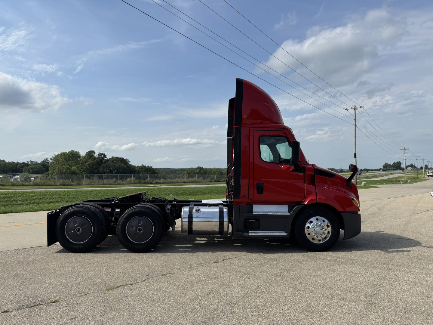 Freightliner Cascadia 116 day cab tractor from side view showing red cab, black dual rear axles, fuel tanks, and wheels.
