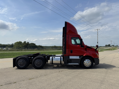 Freightliner Cascadia 116 day cab tractor from side view showing red cab, black dual rear axles, fuel tanks, and wheels.