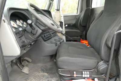 Interior of a 2013 International PROSTAR+ 113 daycab showing steering wheel, dashboard gauges, manual transmission shifter, two front bucket seats, pedal cluster, and worn floor mats.