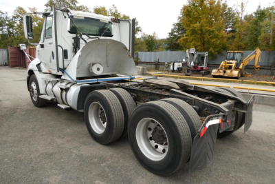 Truck chassis with cab showing fifth wheel and dual rear axles, International ProStar sleeper cab, no trailer attached, yard with equipment in background.
