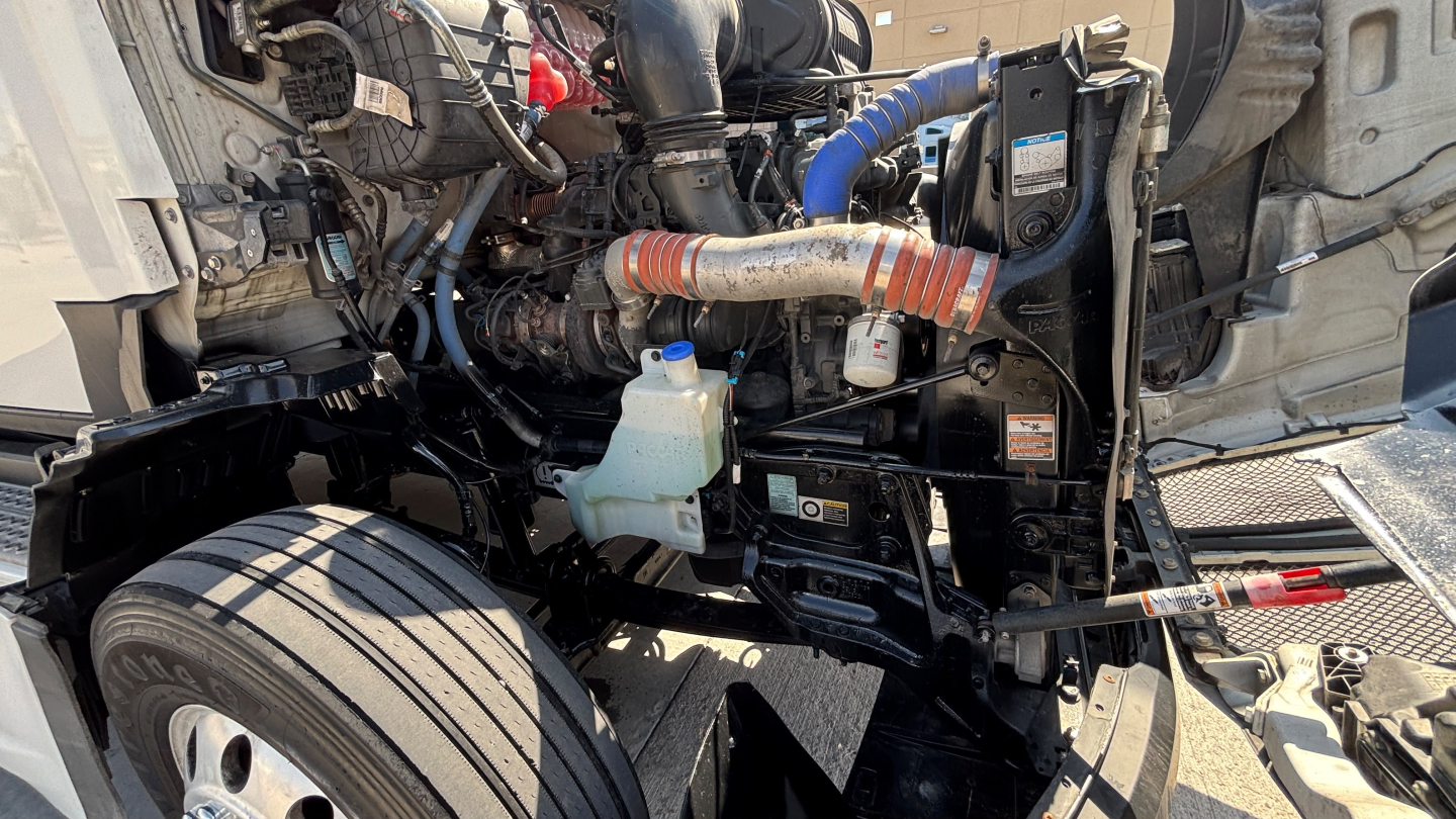 Kenworth T680 engine bay showing coolant reservoir, air intake hoses, and various wiring harnesses in front area.