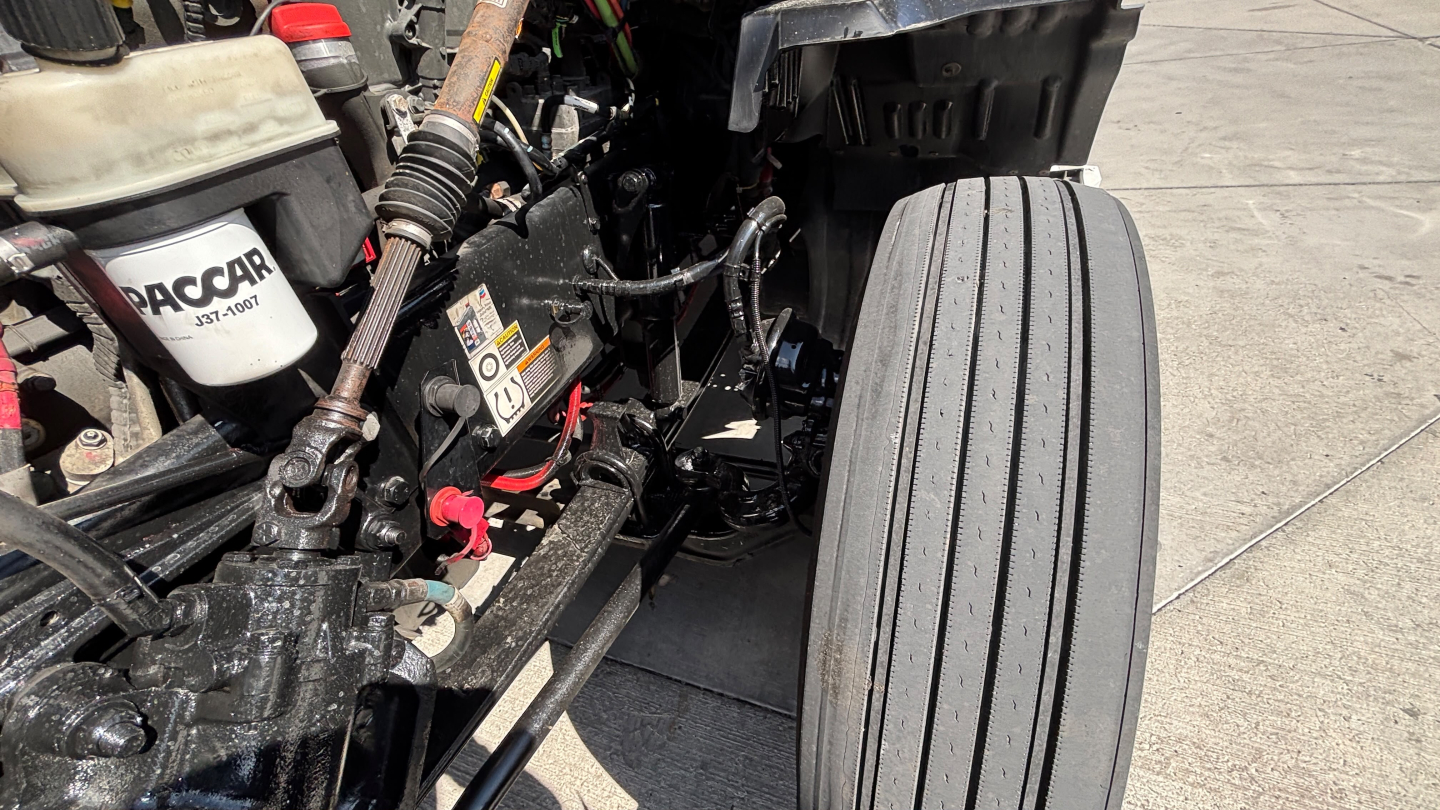 Kenworth truck cab and chassis showing front wheel and engine bay area with hoses and components visible.
