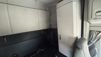 Cab interior of a Kenworth T680 sleeper cab showing a vertical fridge or cabinet, with light gray upholstery and a small door handle.