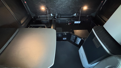 Interior cab space of a 2024 Kenworth T680 with a sleeper, showing a small kitchenette/icebox area and bed surface, dim lighting, and cab wall panels.