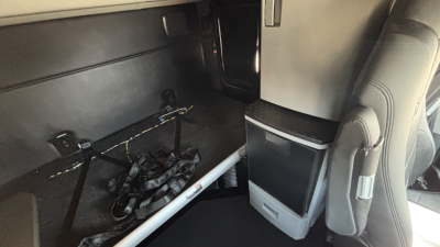 Truck cab interior showing sleeper area with storage cabinet and harnesses; limited view of dash area and vertical support.