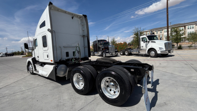 Kenworth T680 tractor rear view showing dual rear axles and fifth-wheel connection, side sleeper cab, white exterior, in-service used truck yard.
