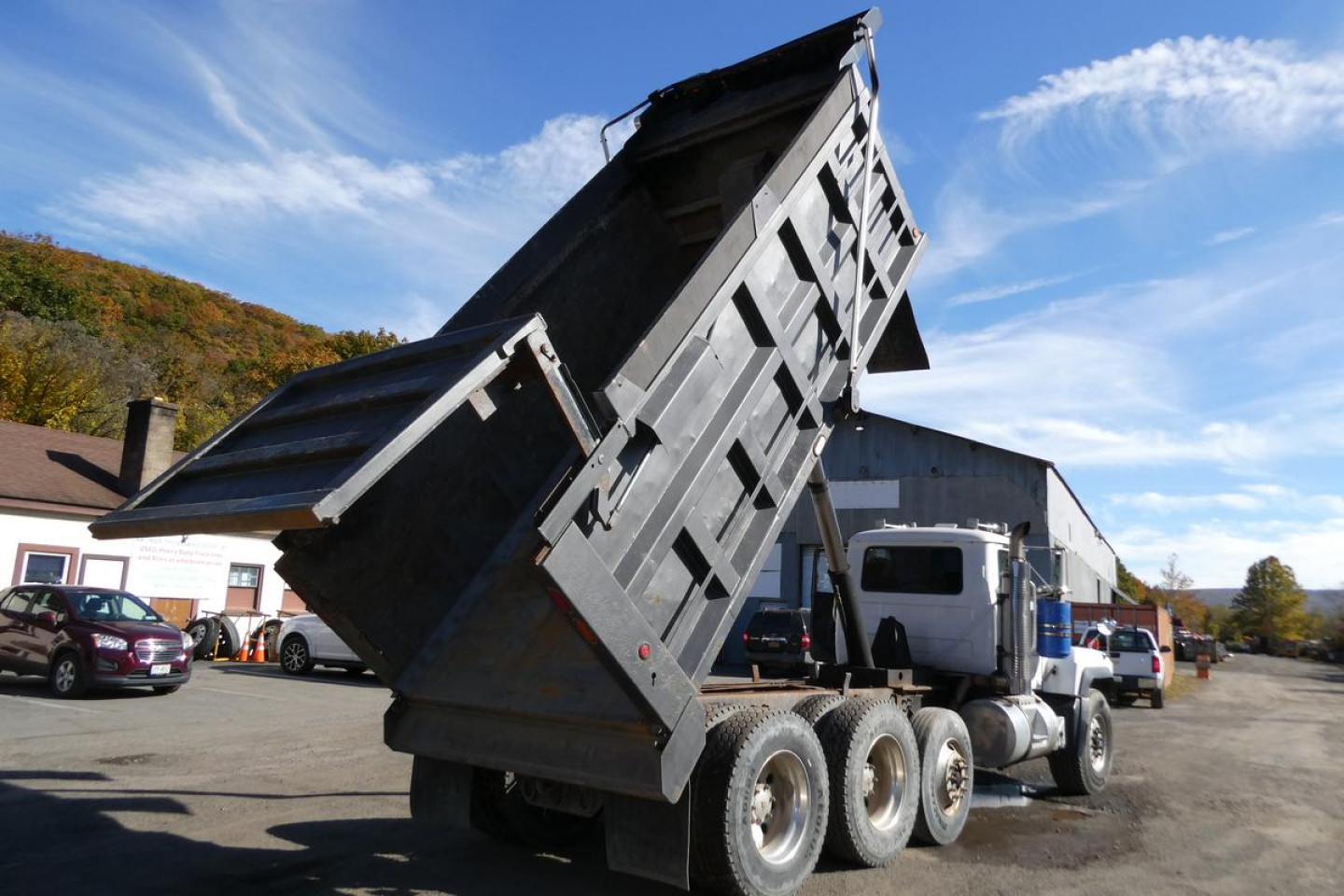 Dump truck in operation showing elevated dump bed on a 2001 Mack RD688S with triple rear axles and hydraulic latch.