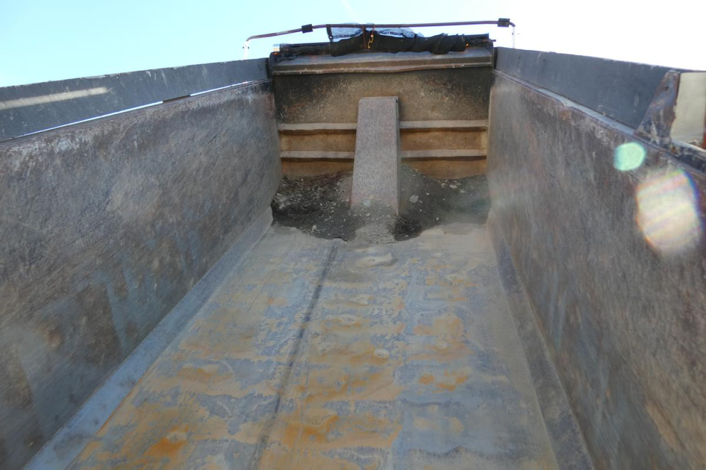 Dump truck bed interior showing worn metal surface and tailgate area with elevated chock.