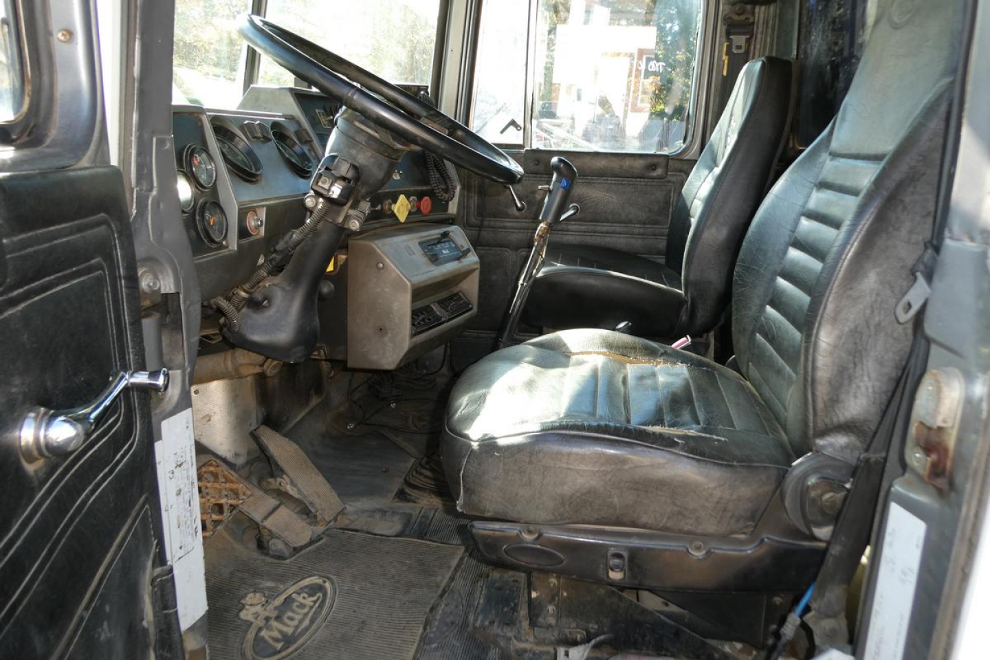 Cab interior of a 2001 Mack RD688S dump truck showing steering wheel, dash with gauges, gear shifter, and two front seats with worn upholstery.
