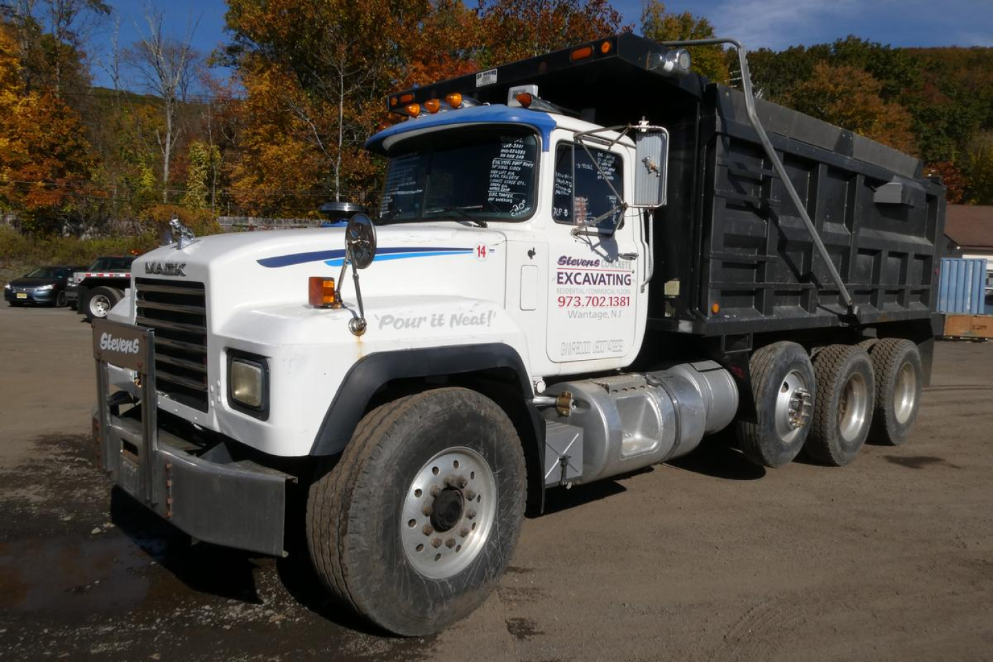 Dump truck showing Mack RD688S with white cab and black dump bed, front grille guard, side text and logo, and multiple axles.