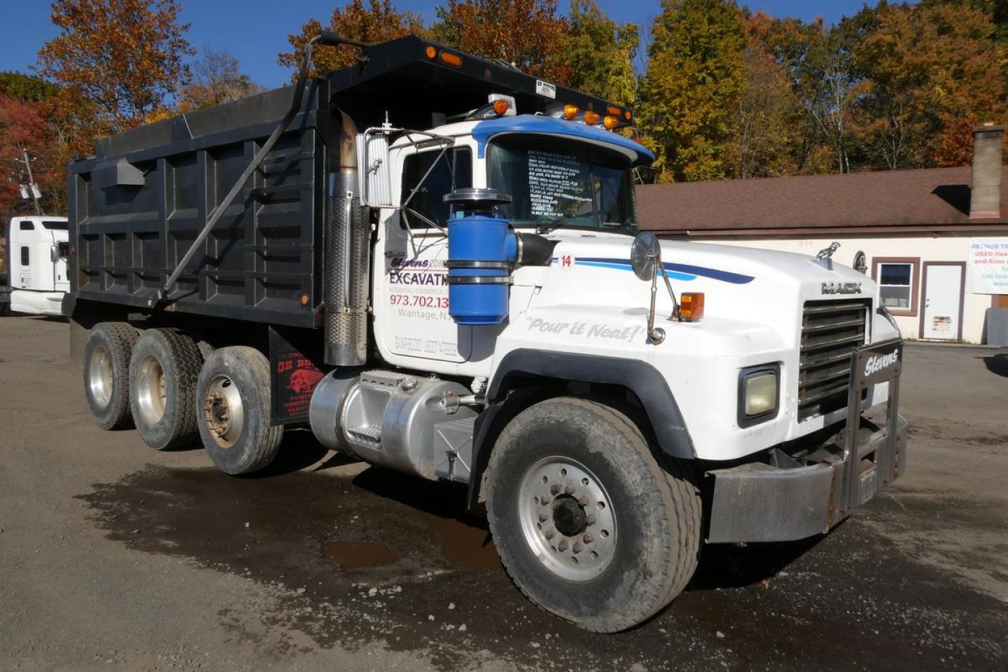 Dump truck showing Mack RD688S front and cab with white paint and blue airfilter, black dump bed, and multiple rear wheels.