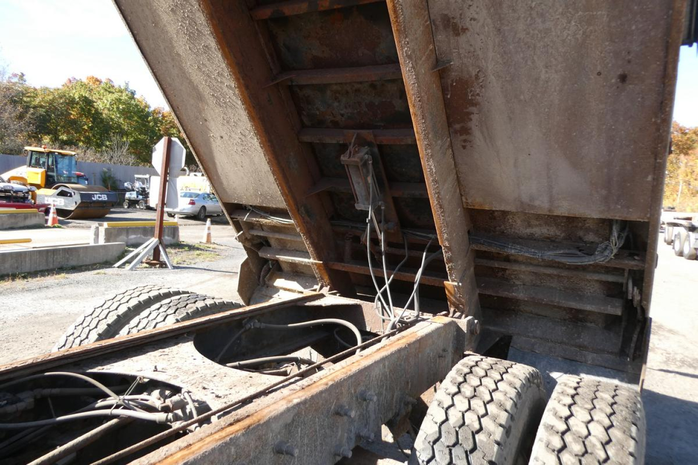 Dump truck bed showing hydraulic ram and wiring in the open cargo area with rusted steel framework.