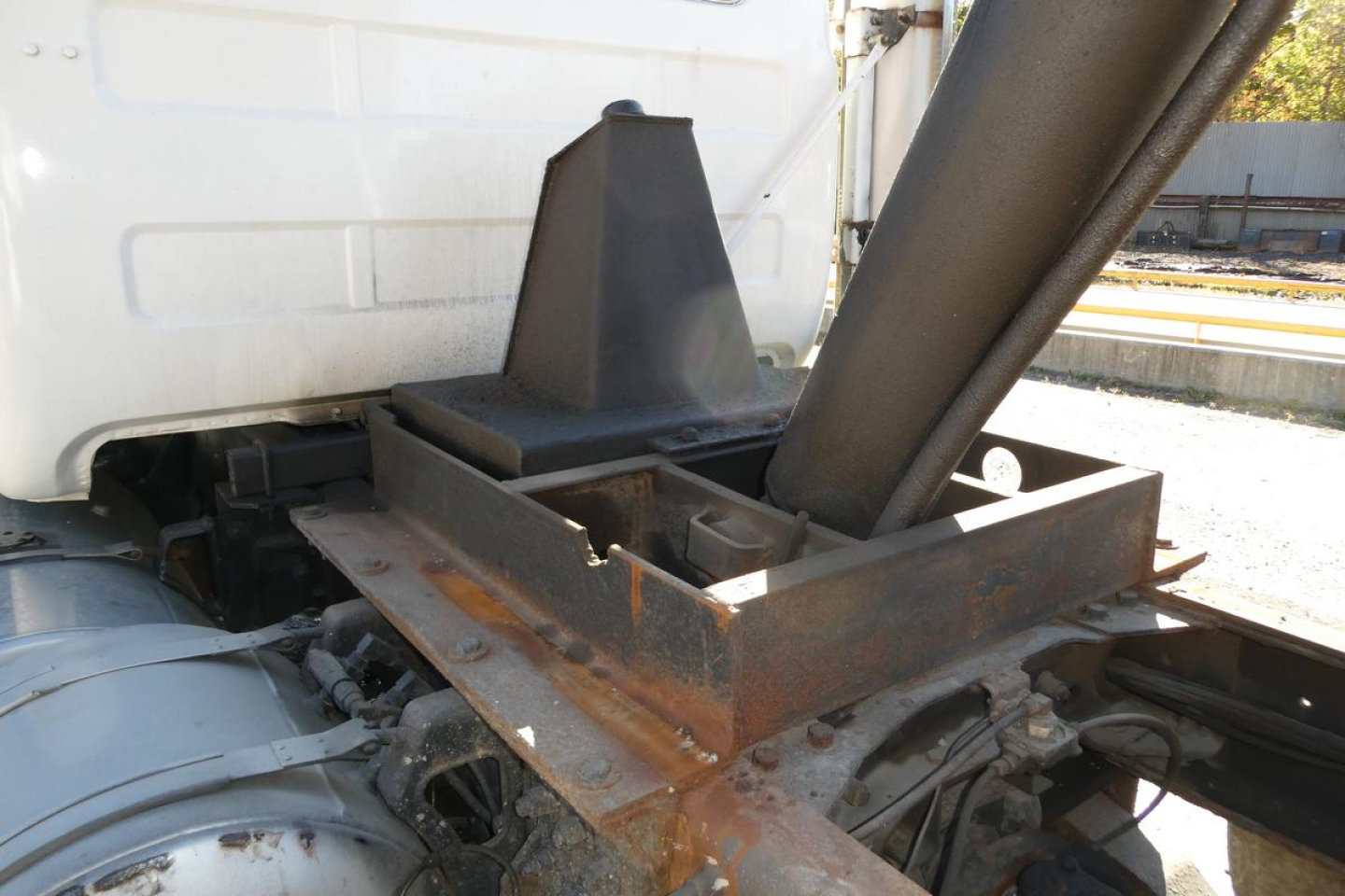Truck chassis and mounting hardware near the cab of a 2001 Mack RD688S dump truck showing a rust-colored frame, hydraulic components, and a metal support structure.