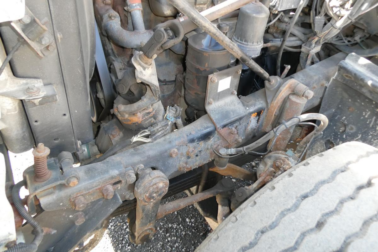 Mack RD688S truck engine bay with exposed frame, hoses, and components; visible are steering linkage, battery area, and front suspension components amidst grime.
