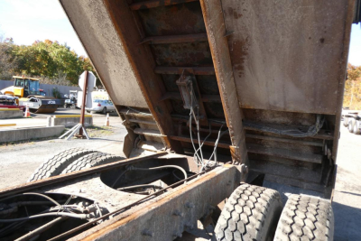 Dump truck bed showing hydraulic ram and wiring in the open cargo area with rusted steel framework.