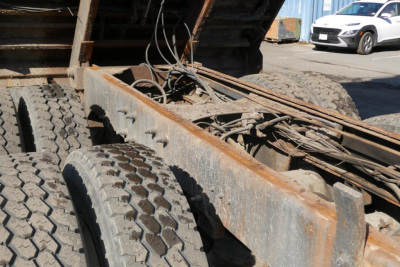Mack RD688S dump truck chassis and tandem rear wheels showing rusted frame and tires with a white car in background.