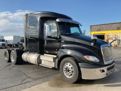 Truck side view showing International LT cab with glossy black paint, chrome grille, sleeper cab, dual rear axles, aluminum fuel tanks, and side steps.
