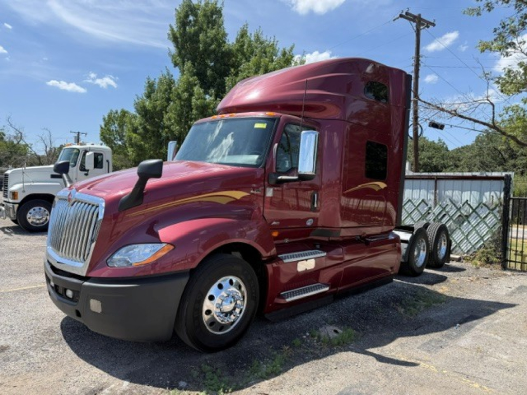 International LT Series sleeper tractor showing cab with maroon paint and chrome wheel covers. Front grille with bumper, side mirrors, and fuel tanks visible.