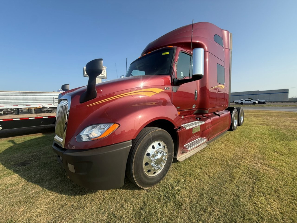 Truck with maroon cab showing International LT625 badge, ventilation vents, side steps, chrome fuel tanks, and headlights.