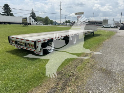 Drop deck trailer showing rear and side, with legal lights and reflective tape; visible branding on bumper; long flatbed with dual rear axles in-use.