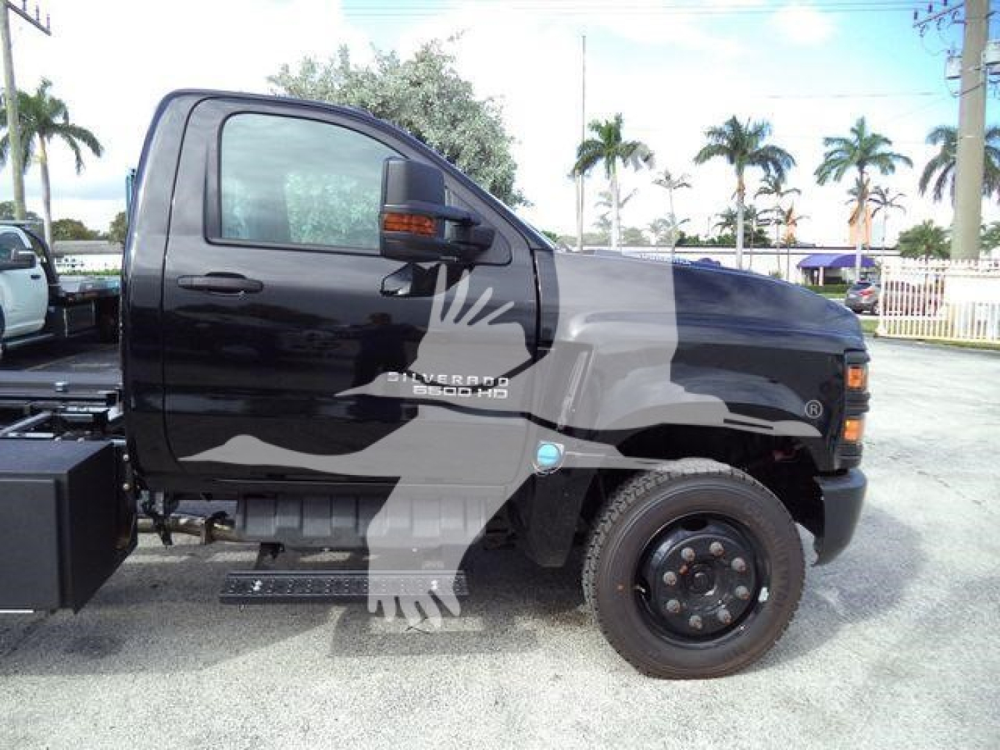 Side view of a black 2023 Chevrolet Silverado 6500HD rollback truck showing cab, door, and front wheel with running board and decals.