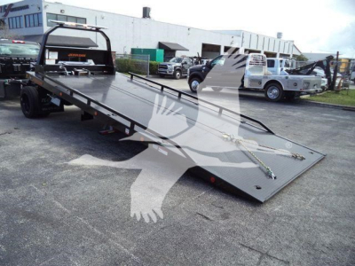 Flatbed tow truck with a long low-ratio ramp in a parking lot; text on the truck reads Chevrolet Silverado 6500HD and various equipment on bed