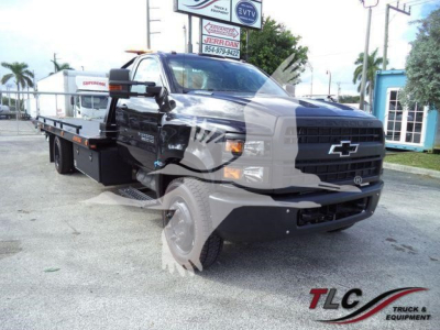 Chevrolet Silverado 6500HD rollback tow truck in showroom setting showing flatbed and black front grille with Chevrolet emblem.