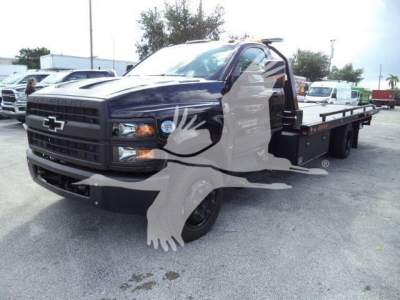 Chevrolet Silverado 6500HD rollback truck showing front grille with Chevy emblem and large flatbed, black color, in-service vehicle.