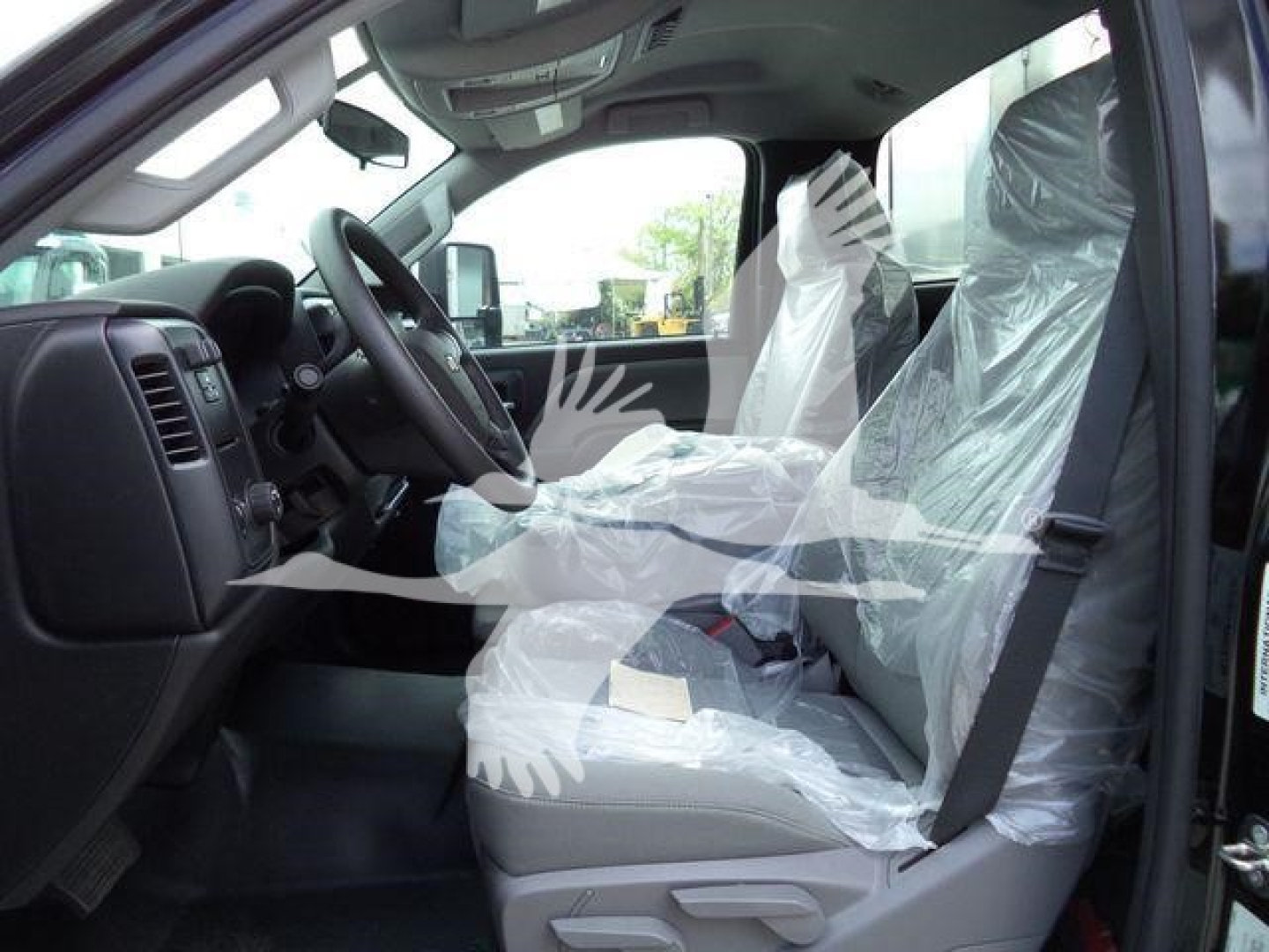 Interior of a Chevrolet Silverado 6500HD cab with plastic seat covers, showing driver seat, steering wheel, and front passenger seat.