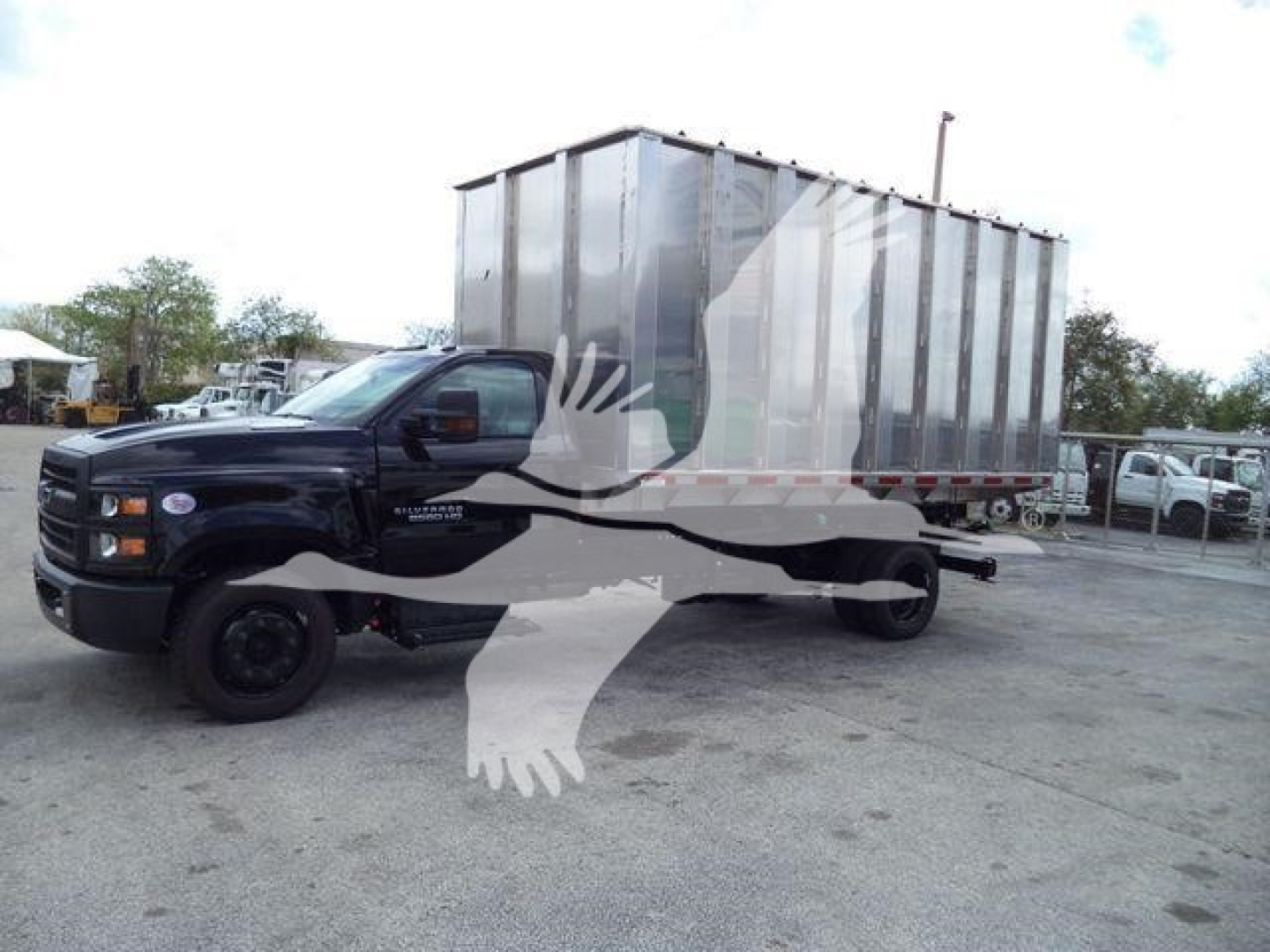 Truck with a large silver trailer/chipper container on a black Chevrolet Silverado 6500HD chassis; decals and stock number may be visible on the vehicle.