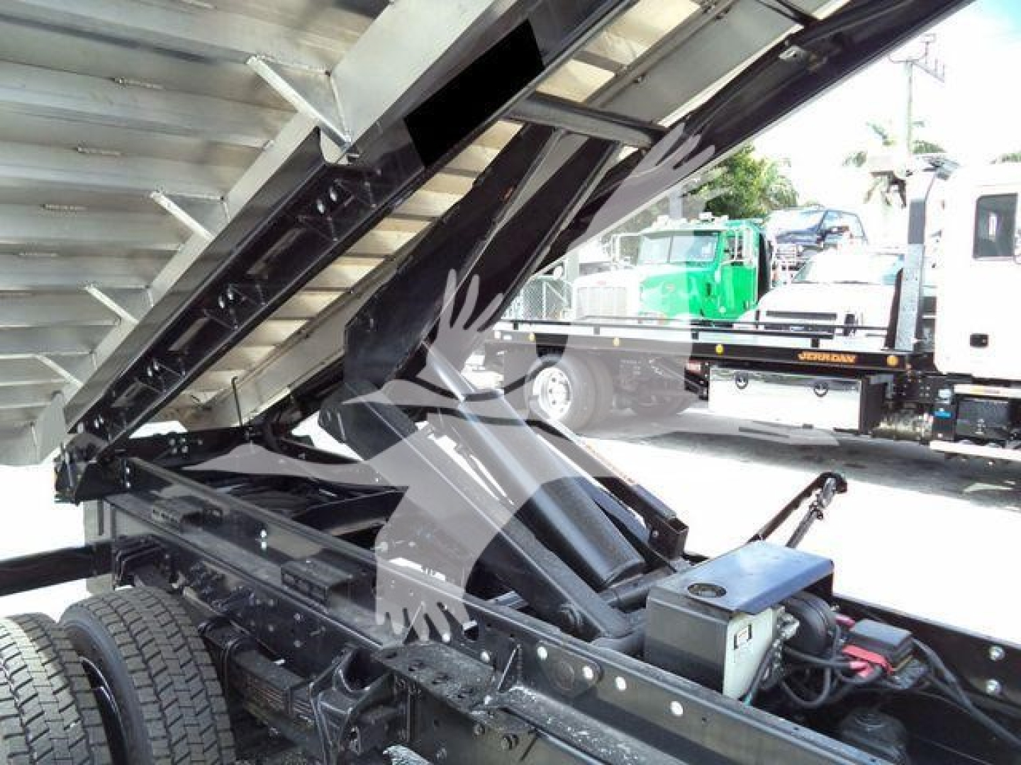 Truck chassis with hydraulic dump bed elevated, showing steel frame, hydraulic cylinders, and undercarriage components.