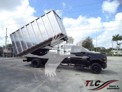 Chevrolet Silverado 6500HD dump truck in a tilted bed position, black cab with long chassis, large silver dump body raised for dumping.