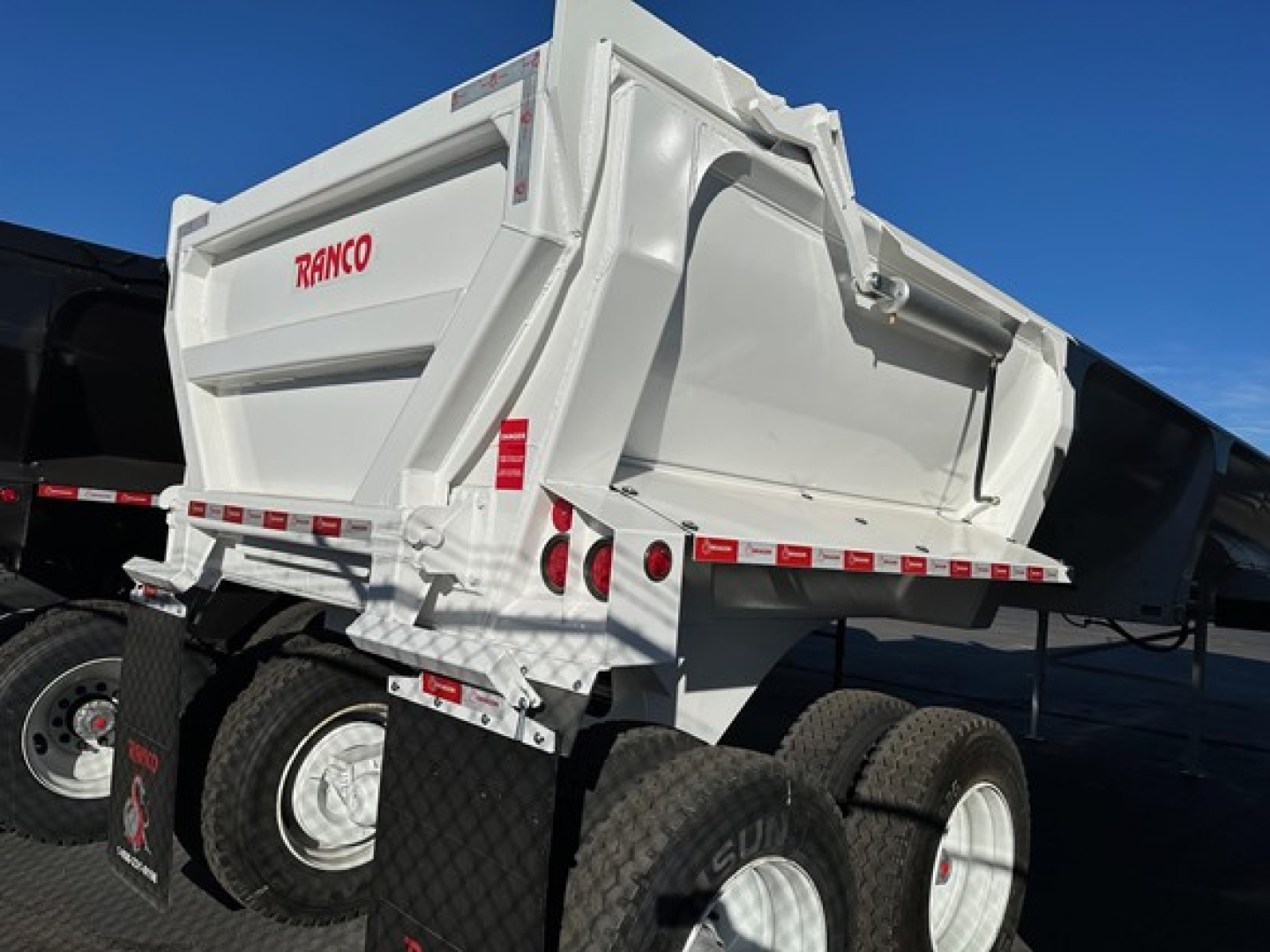 Ranco ED26-34 dump trailer in white showing RANCO logo on side and rear, dual axle wheels, and reflective safety decals.