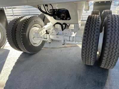 Trailer undercarriage with dual axles and leaf spring suspension, EZ-connect hoses, and large tires. Visible is white painted chassis and rear axle assembly with bolts and brackets.