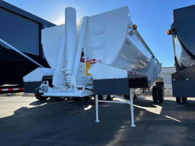 Dump trailer with Ranco Ed26-34 model, white aluminum body, raised front landing gear, parked on asphalt with other trailers nearby. Visible labels and warning decals on side.