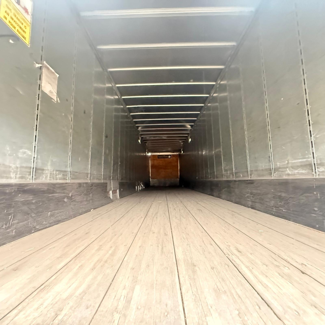 Trailer interior showing wooden floor and side walls with entry at far end; linear ceiling lights; clean, empty dry van trailer interior.