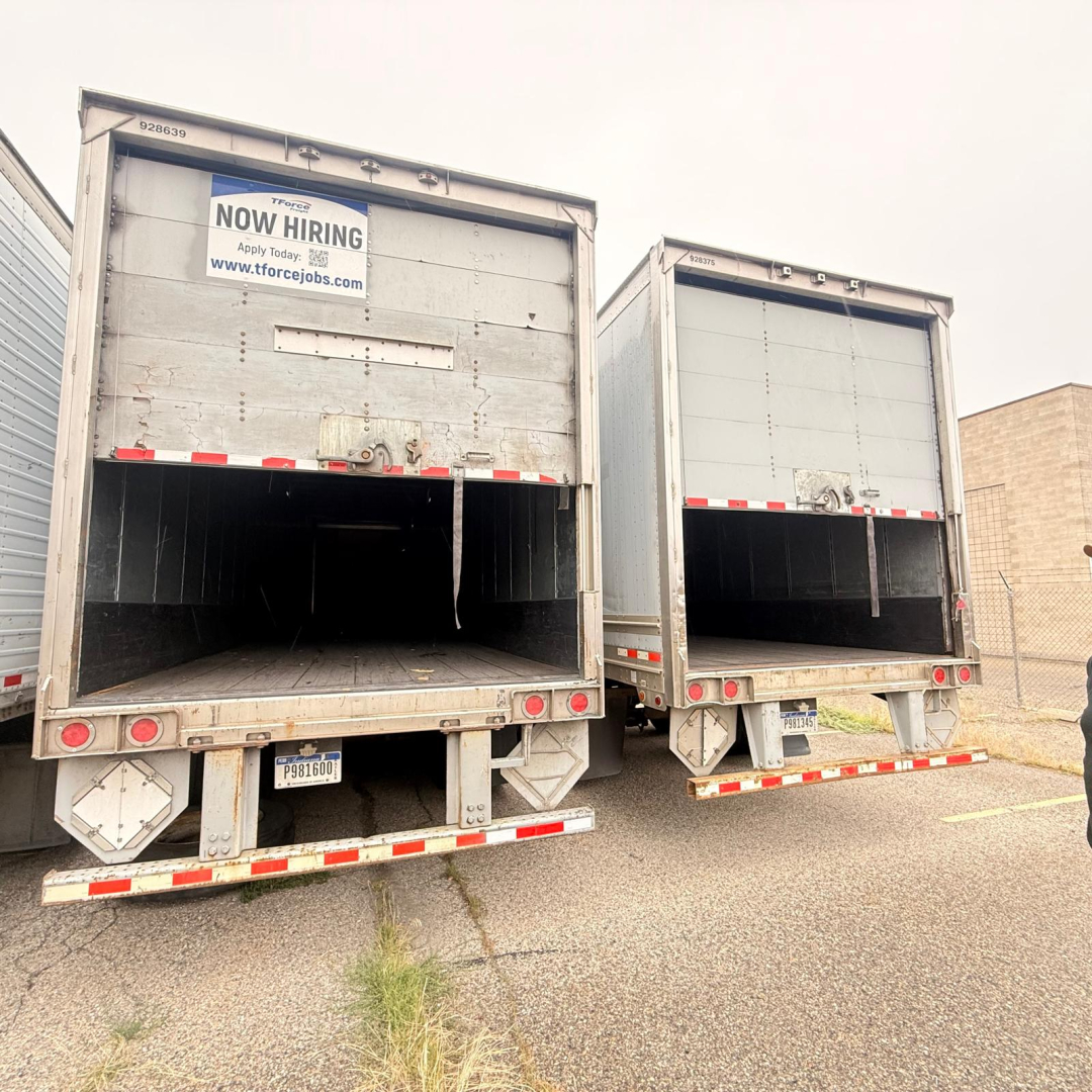 Two grey dry-van trailers with open rear doors, Now Hiring sign on left door, rear bumper lights, and license plate areas visible.
