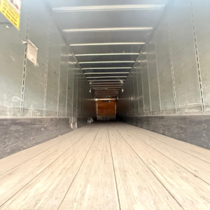 Trailer interior showing wooden floor and side walls with entry at far end; linear ceiling lights; clean, empty dry van trailer interior.