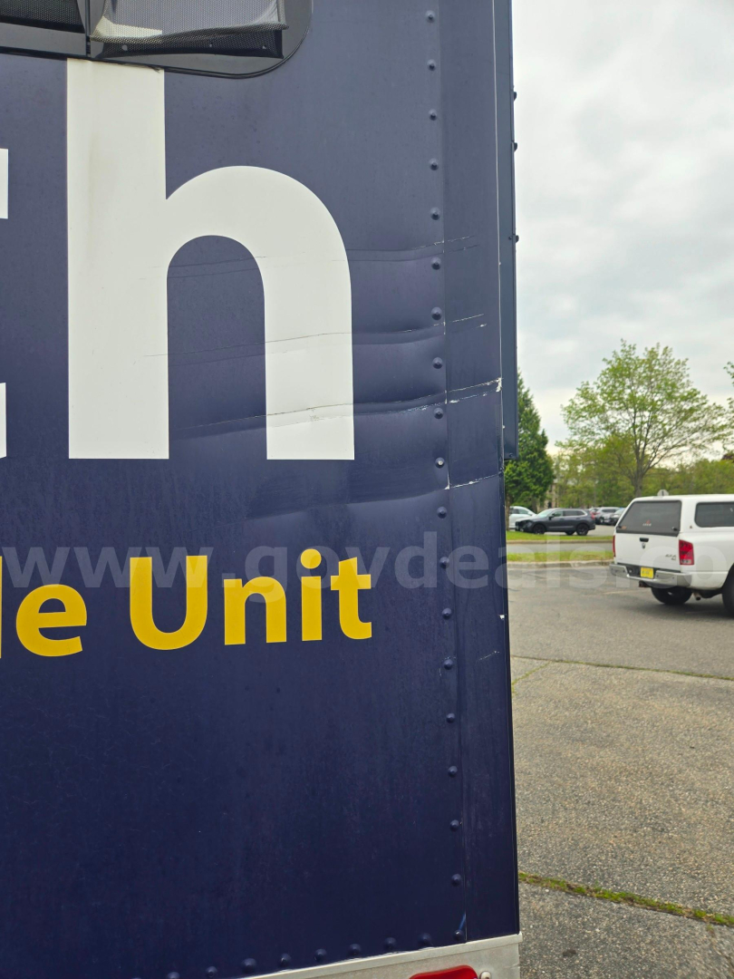 Truck side panel of a Freightliner M2 with partial large white lettering and a white pickup in the distance.