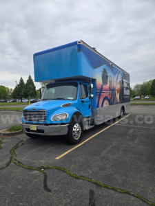 Box truck 2019 Freightliner M2 side/driver view showing blue cab and blue cargo box with graphic wrap