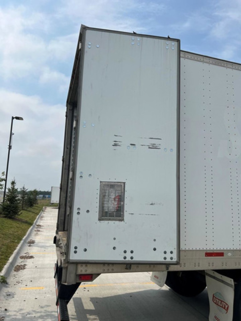 Trailer rear left vertical panel with small access door and riveted metal, light gray, on a white trailer. Residue marks around door and rear area.