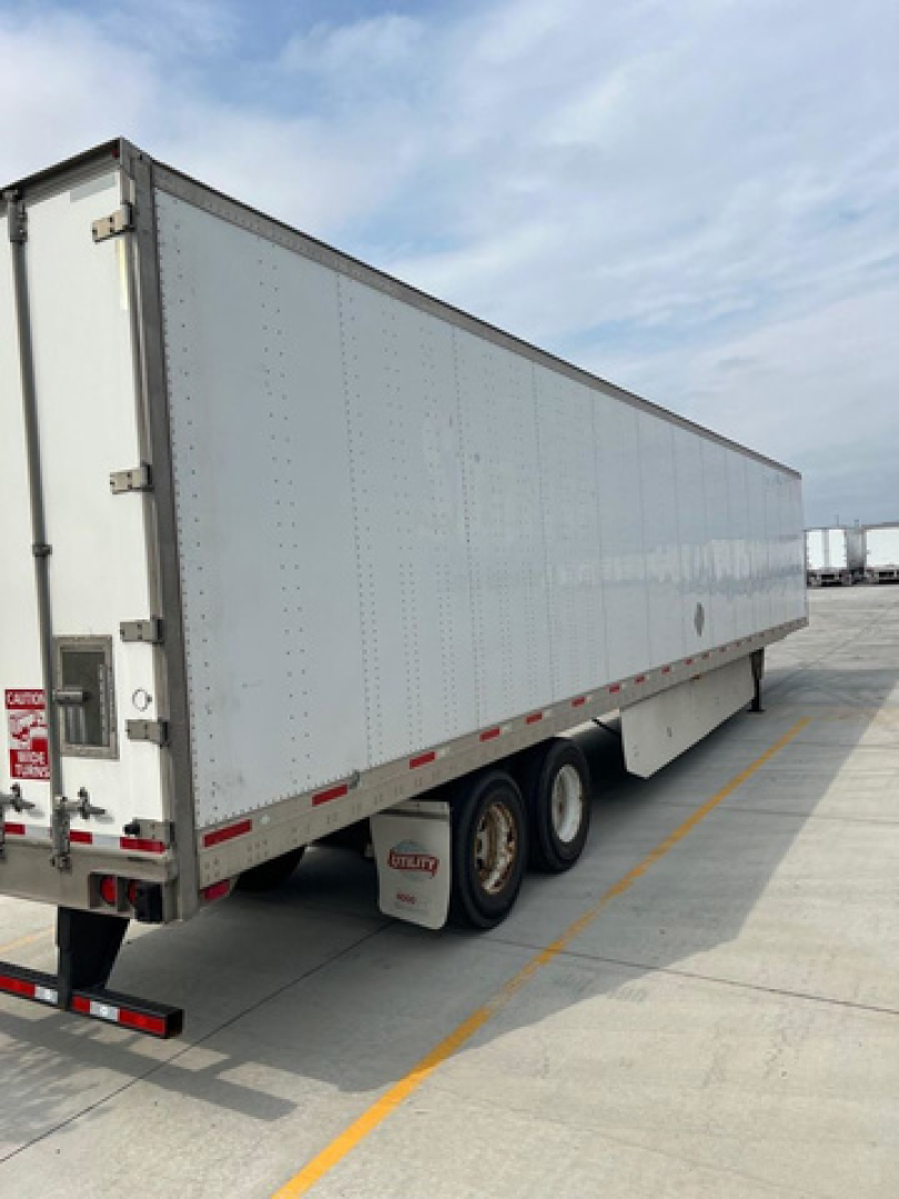 Trailer side view of a long white utility van trailer with dual rear axles and reflective striping along bottom edge.