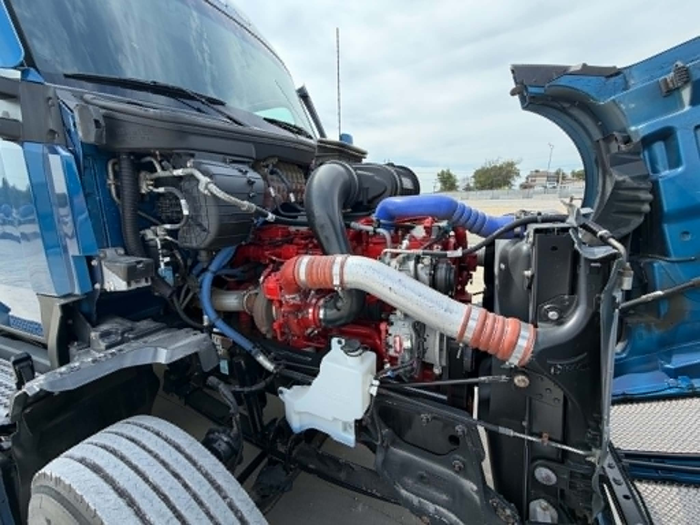 Kenworth T680 engine bay showing red engine, intercooler piping, hoses, and open hood with blue exterior.