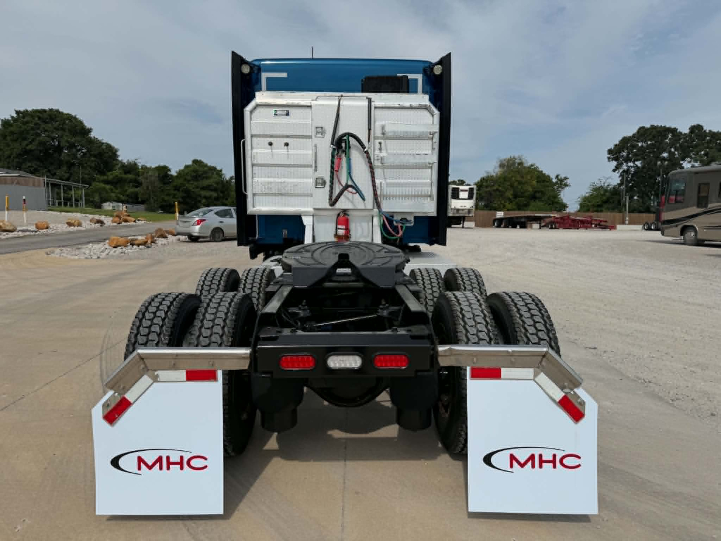 Kenworth T680 rear view showing tractor chassis, dual rear axles, MHC mudflaps, and white storage boxes with hydraulic lines.