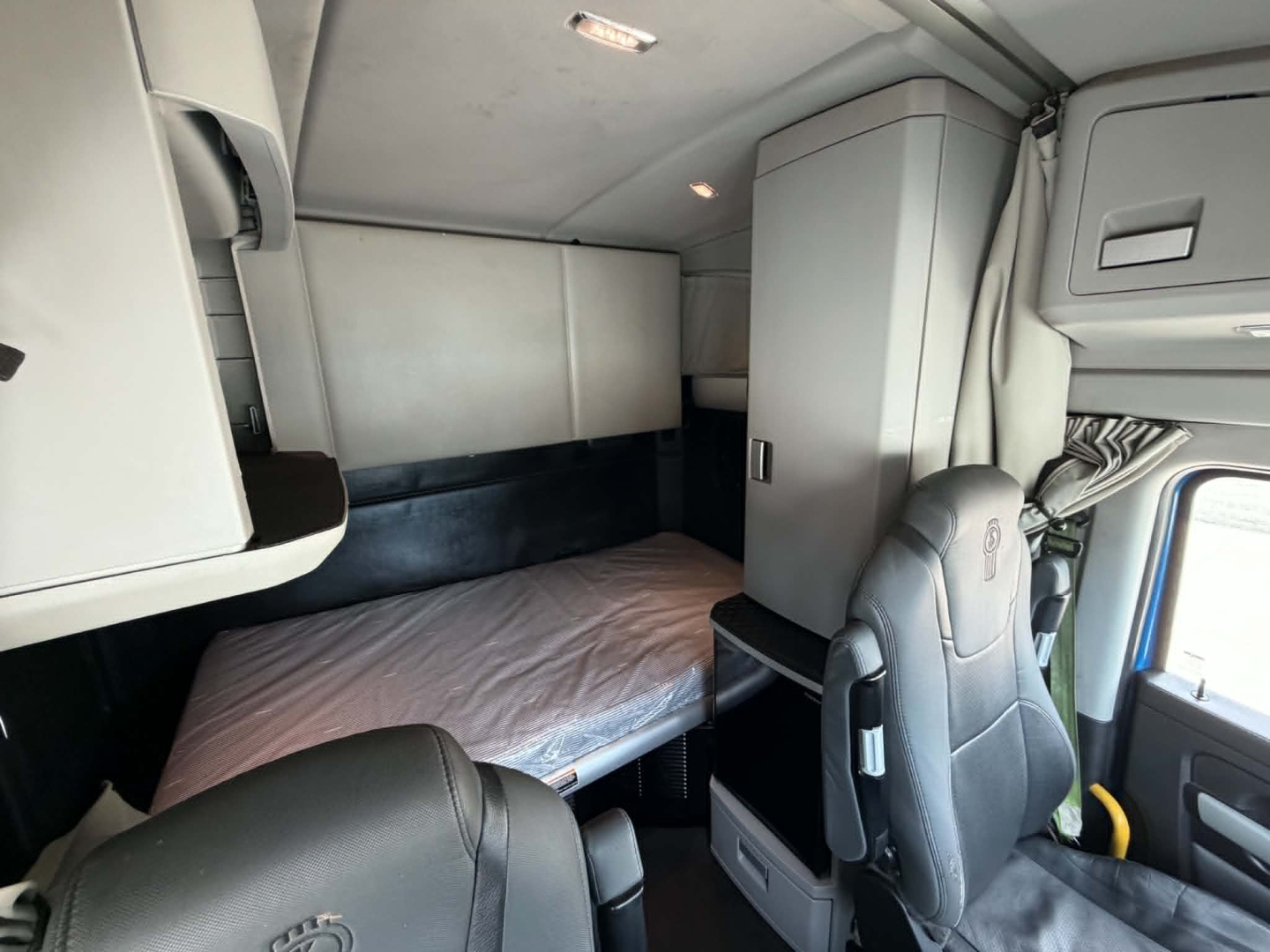 Kenworth T680 sleeper cab interior showing bunk bed and driver's seat with overhead cabinets.