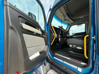 Kenworth T680 cab interior view with open driver door; steering wheel, dashboard, and yellow handrails visible.