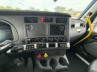 Dashboard of Kenworth T680 truck showing center console with various knobs, switches, cup holders, and a yellow grab handle visible on the passenger side.