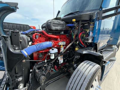 Kenworth T680 engine bay view showing red engine with blue turbo hoses and various cables and components.