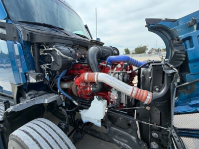 Kenworth T680 engine bay showing red engine, intercooler piping, hoses, and open hood with blue exterior.